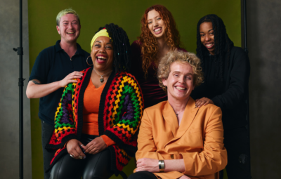 A diverse group of five people smiling and posing against a green background.