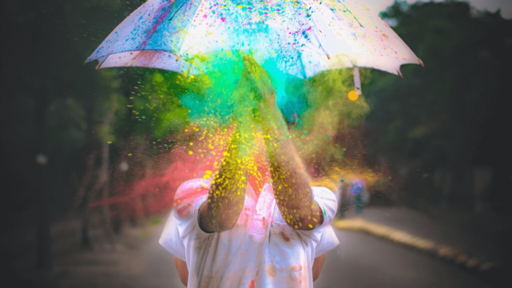 Person holding a colorful umbrella as vibrant powder explodes around, creating a festive, rainbow effect.