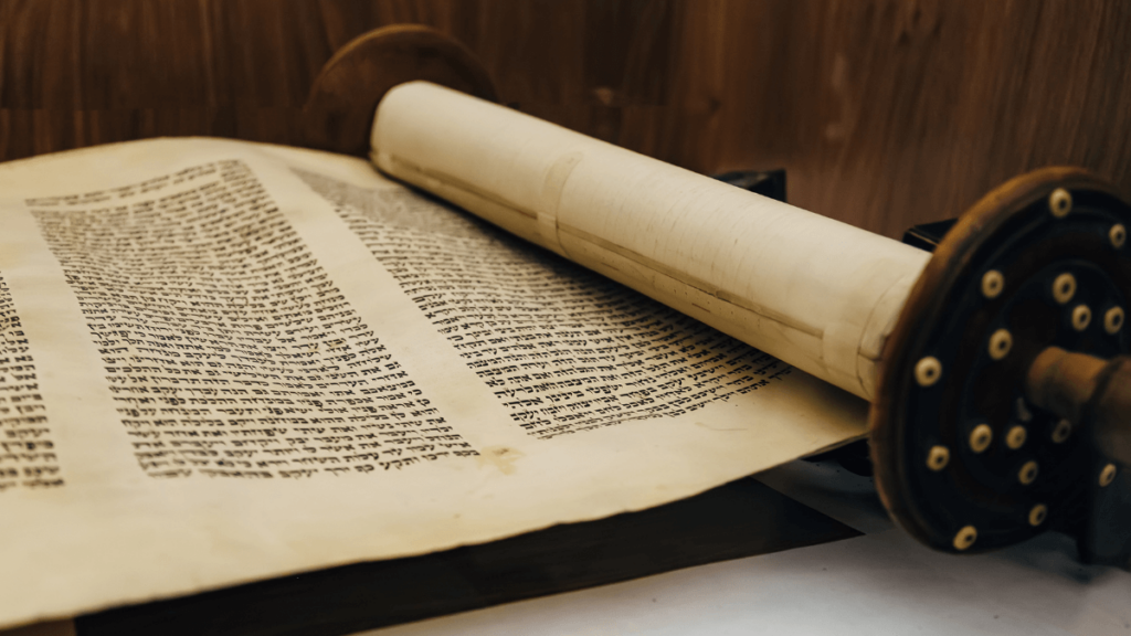 A partially unrolled Torah scroll with Hebrew text on a wooden table.