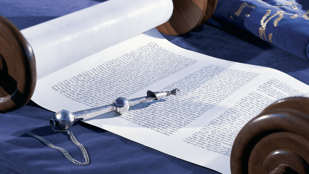 Open Torah scroll on blue fabric with a yad pointer resting on the parchment.