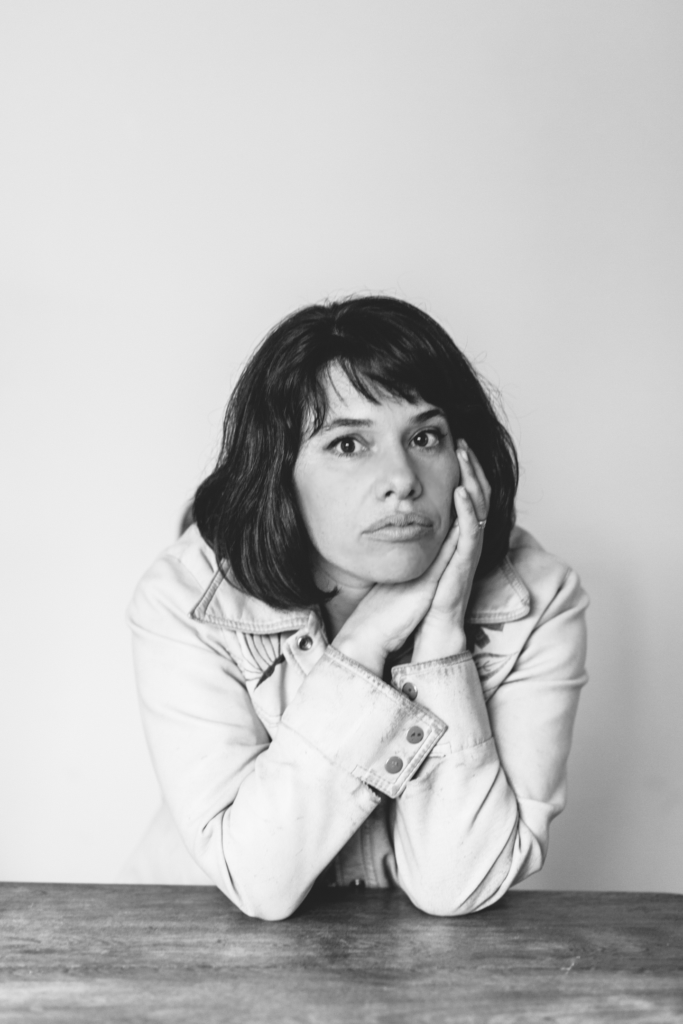 Black-and-white photo of a person with a thoughtful expression, resting their chin on their hands at a table.