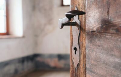 Close-up of a rustic wooden door slightly ajar, with a vintage door handle and blurred interior background.