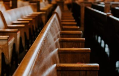 Wooden pews line a quiet, empty church interior with red cushions and soft lighting.