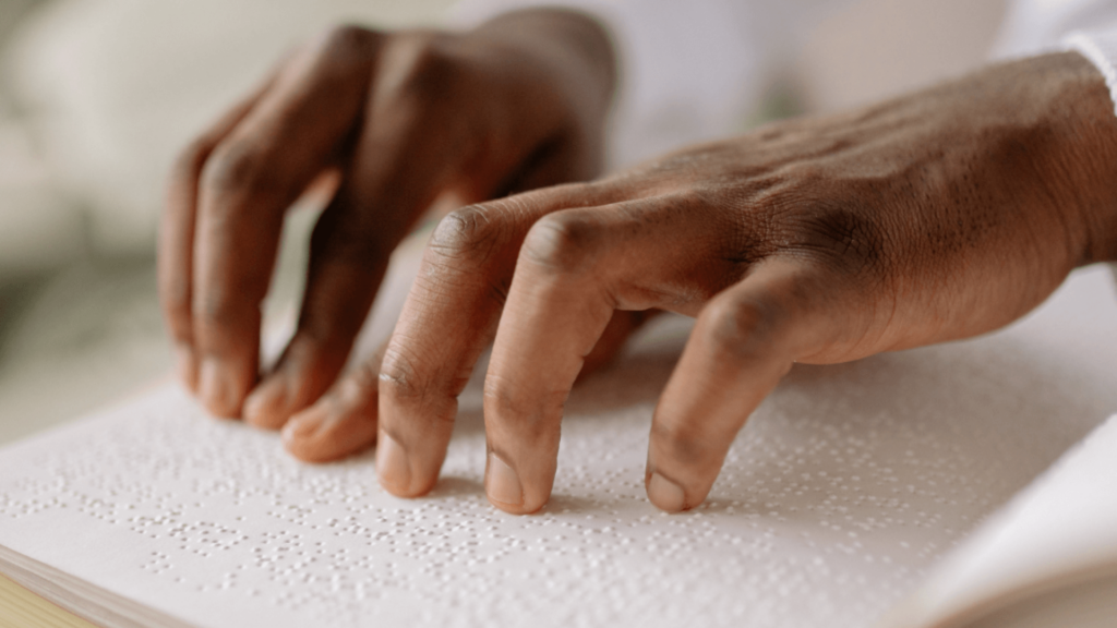 Hands reading braille on a white page.