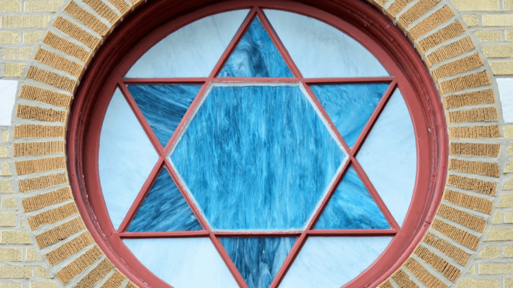 Circular stained glass window with a blue Star of David, framed by red and brown brickwork.
