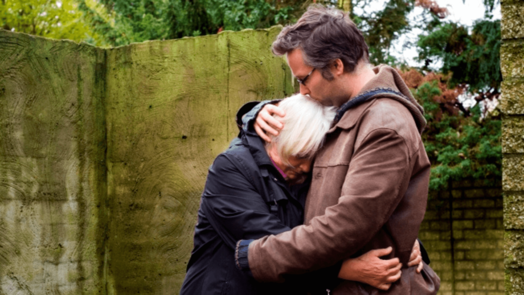 A person comforting another outside, hugging them gently while kissing their head.