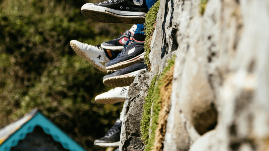 Sneakers hanging over a stone wall, with greenery in the background.