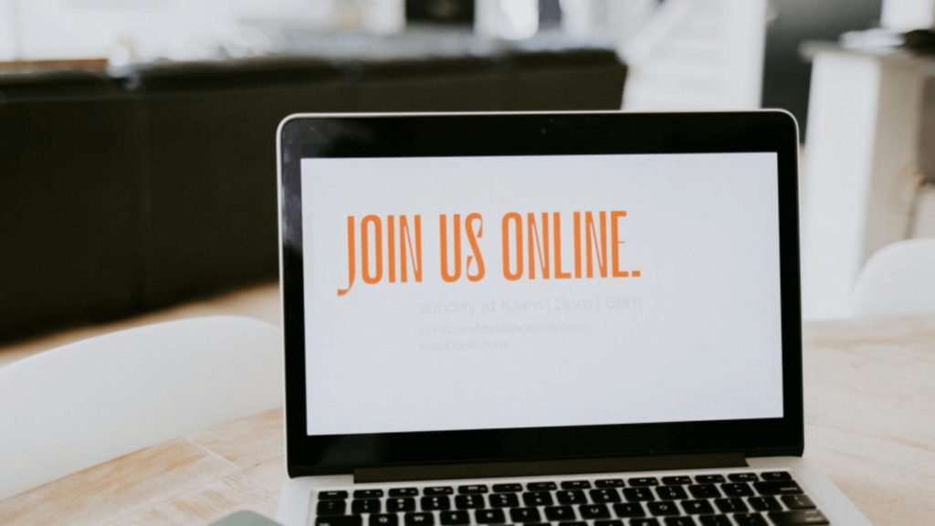 Laptop screen displaying Join Us Online with a white and orange background, on a wooden table.