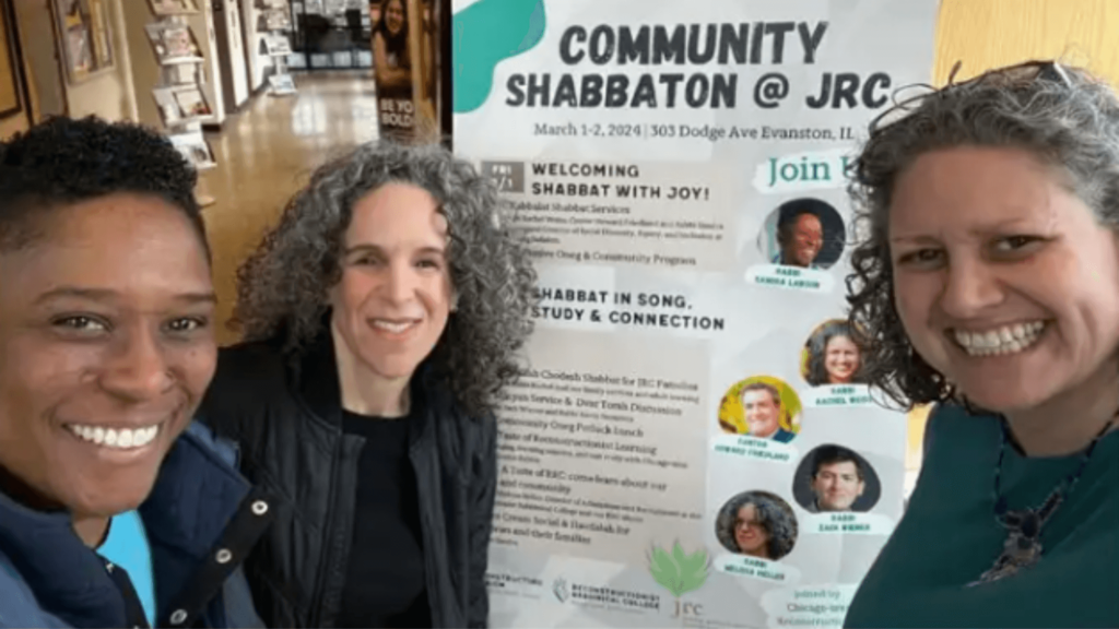 Three rabbis smiling in front of a Community Shabbaton poster at JRC in Evanston, IL.