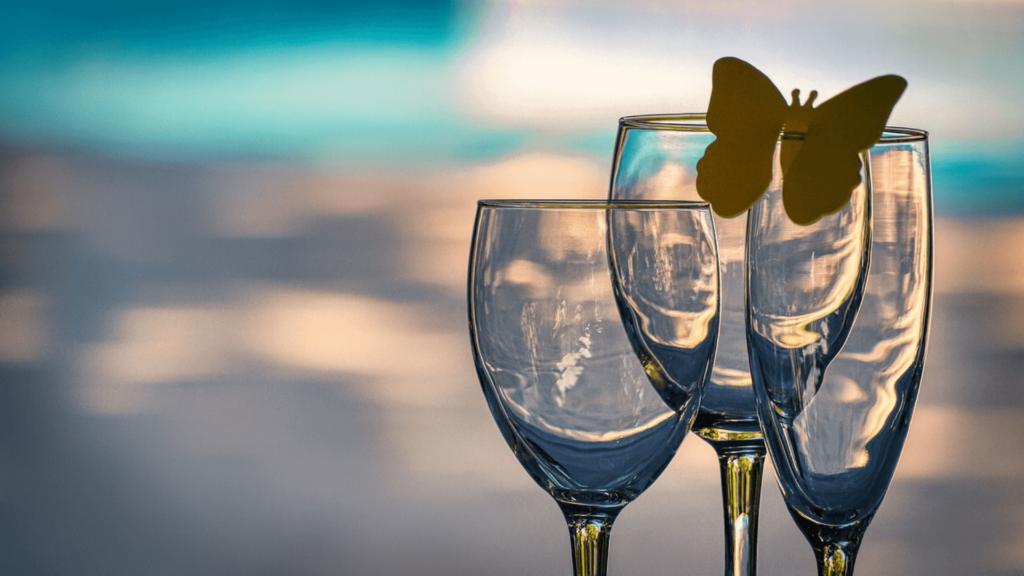 Three empty wine glasses with a paper butterfly decoration, set against a blurred outdoor background.