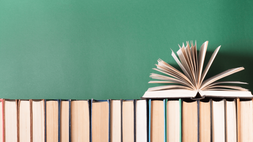 A row of closed books with one open book on top, against a green background.