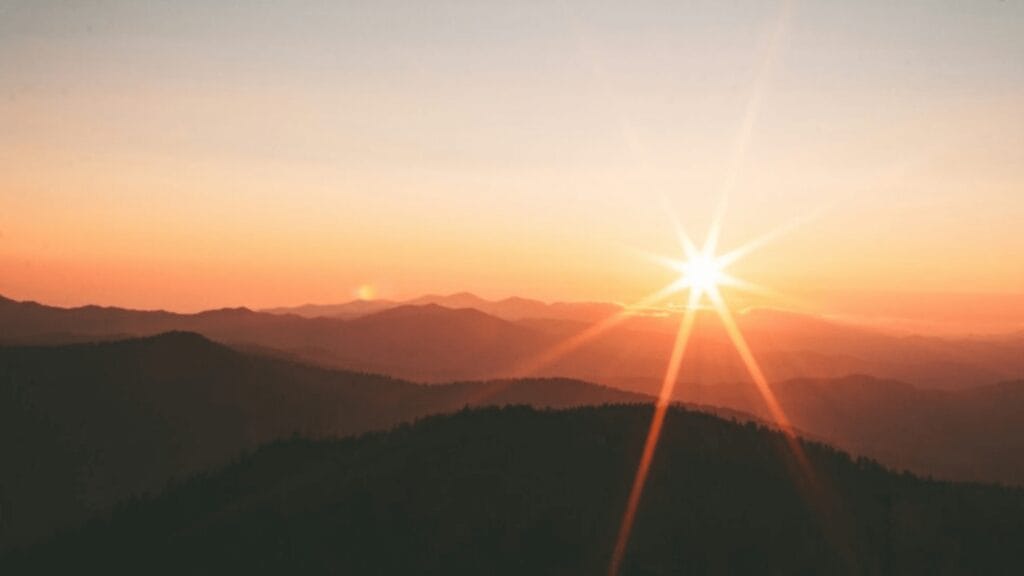 Sunrise over mountain range with layers of silhouettes and an orange sky.