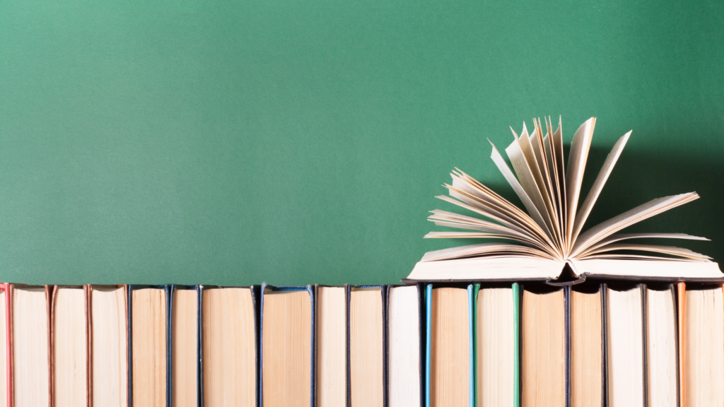 Open book placed on several closed books against a green background.