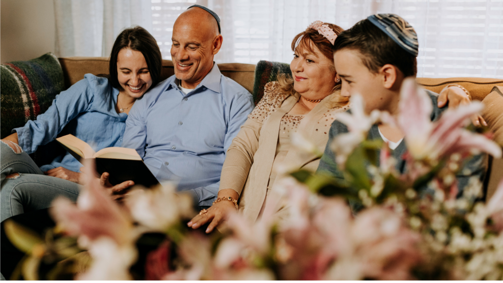 Family sitting on a couch, smiling and reading a book together, with a floral foreground.