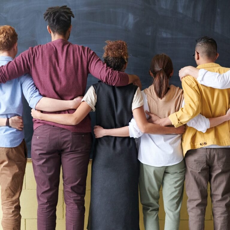 A group of people standing with arms around each other, facing a chalkboard.