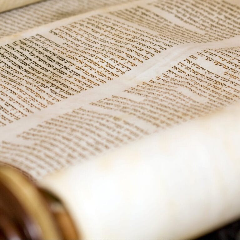 Close-up of an open Hebrew scroll with text in black ink on parchment, partially rolled on wooden handles.