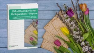 Book titled If God Had Only Given Us Reparations - Dayenu with matzah and spring flowers on a wooden surface.