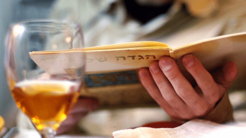 Person holding a Hagaddah, next to a glass filled with wine.