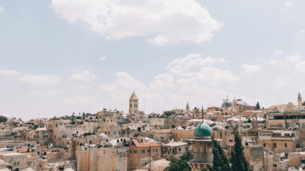 Skyline of an Israeli city with stone buildings, church towers, and domes under a cloudy sky.