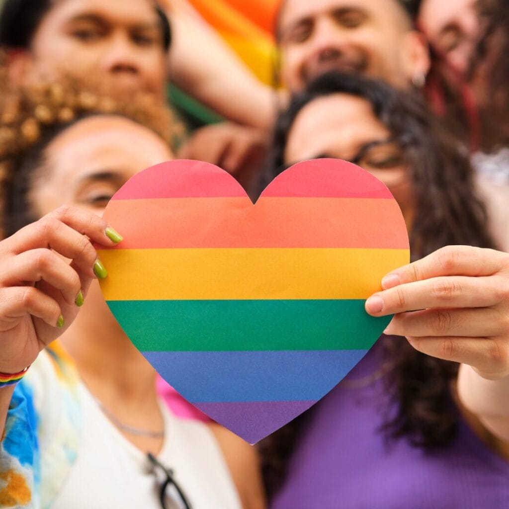 People holding a heart-shaped rainbow flag, celebrating LGBTQ+ pride together.