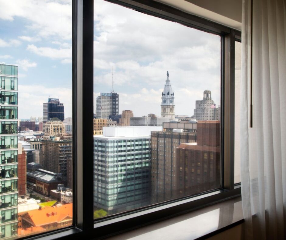 City skyline view from a window, with modern and historic buildings under a partly cloudy sky.