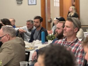 People sitting and listening attentively at a formal indoor event with tables and food.