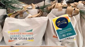Tote bags labeled Service Matters: Israel Summit are displayed on a table with flyers and green onions.