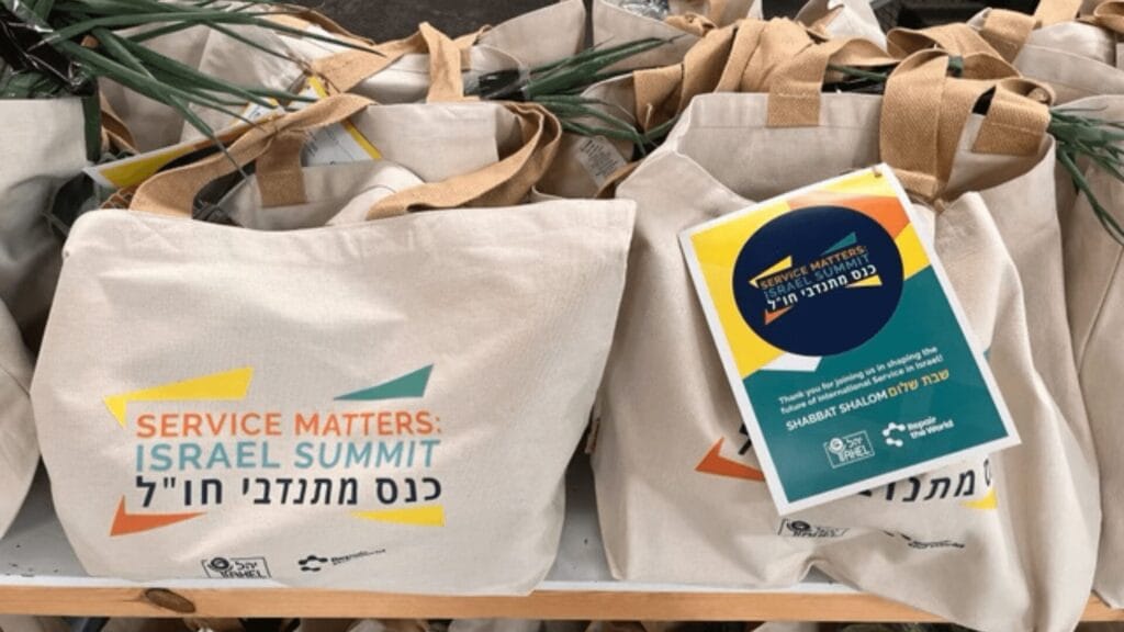 Tote bags full of food with the text "Service Matters: Israel Summit," plus a colorful event flyer in Hebrew and English.