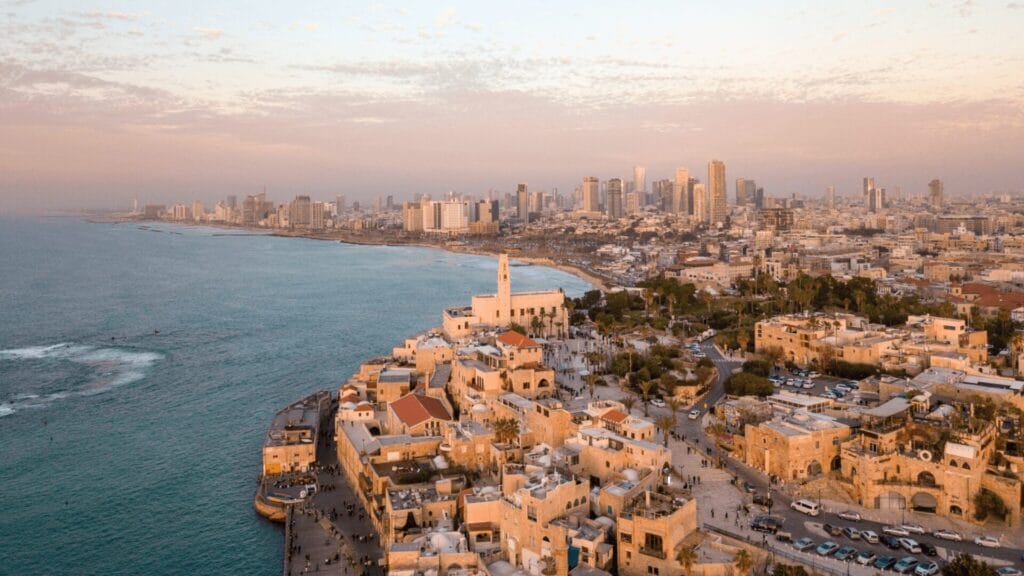 Aerial view of Jaffa’s old port with Tel Aviv’s modern skyline along the Mediterranean coast at sunset.