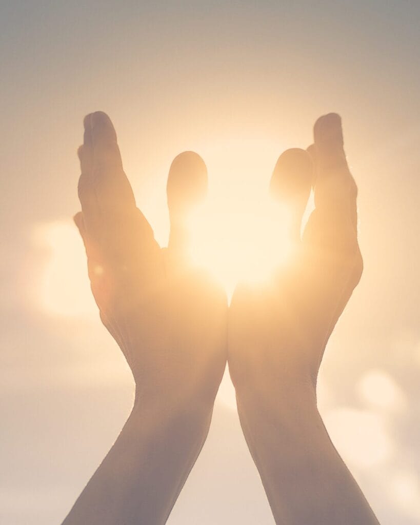 Two hands cupped together reaching toward bright sunlight with a soft, glowing background.