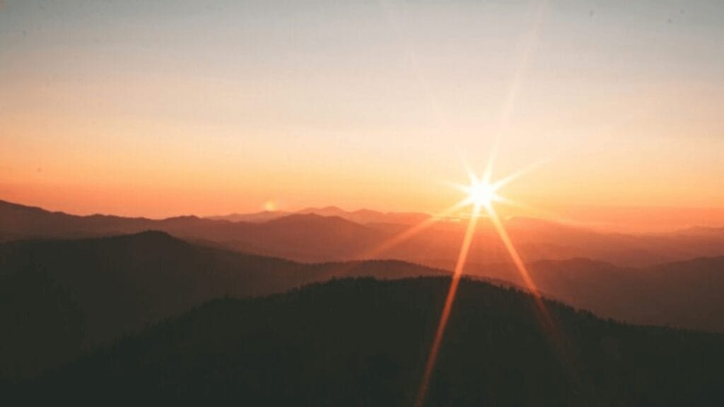 Sunrise over mountain ranges with a warm orange sky and soft light illuminating the landscape.