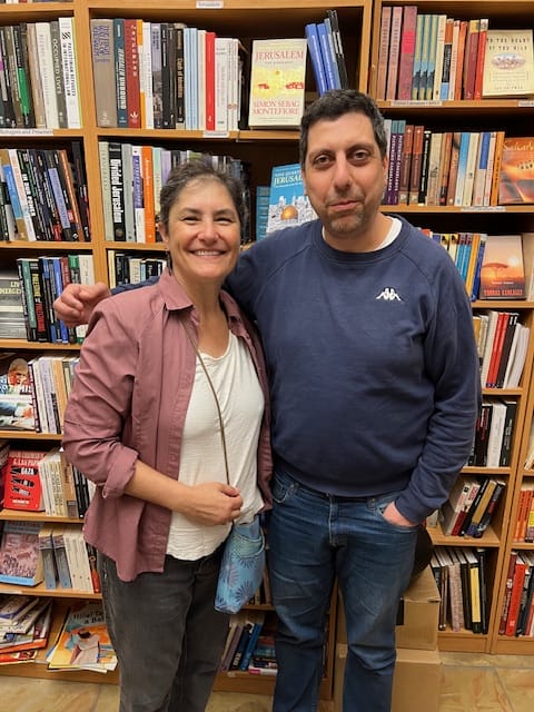Two people standing and smiling in front of bookshelves in a bookstore.