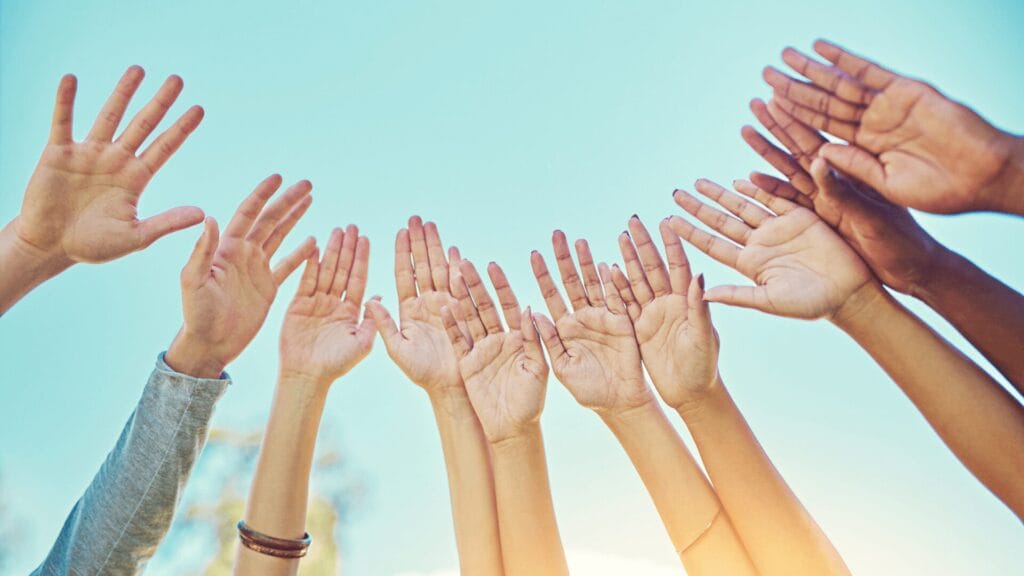 A group of hands with different skin tones reaching up to the sky