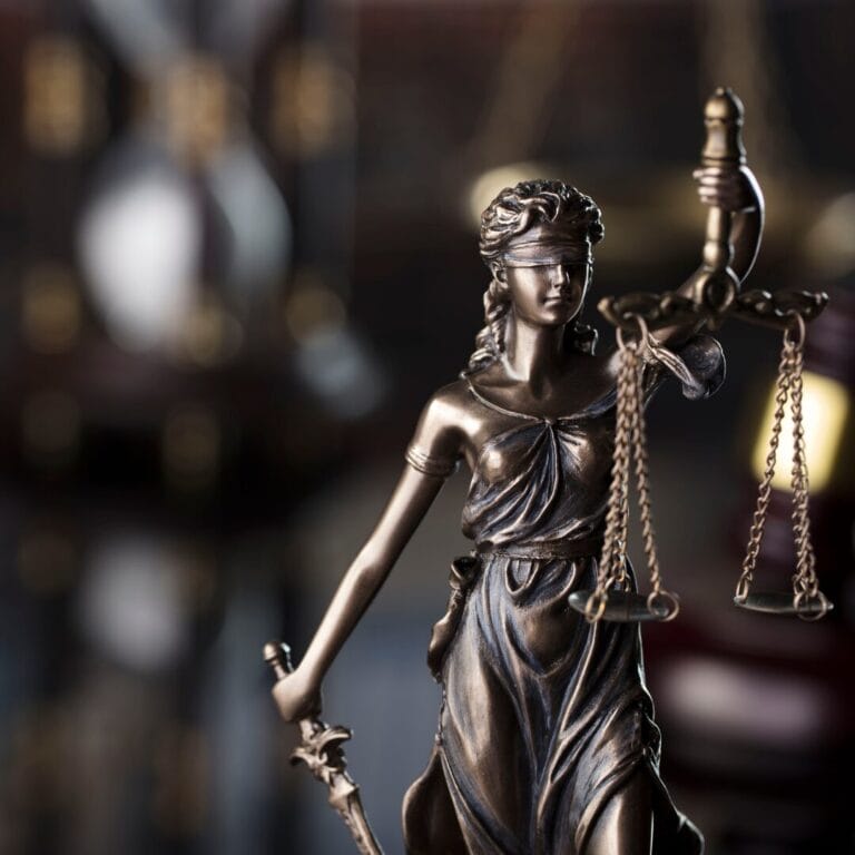 Bronze statue of Lady Justice holding scales and a sword, with a blurred background.