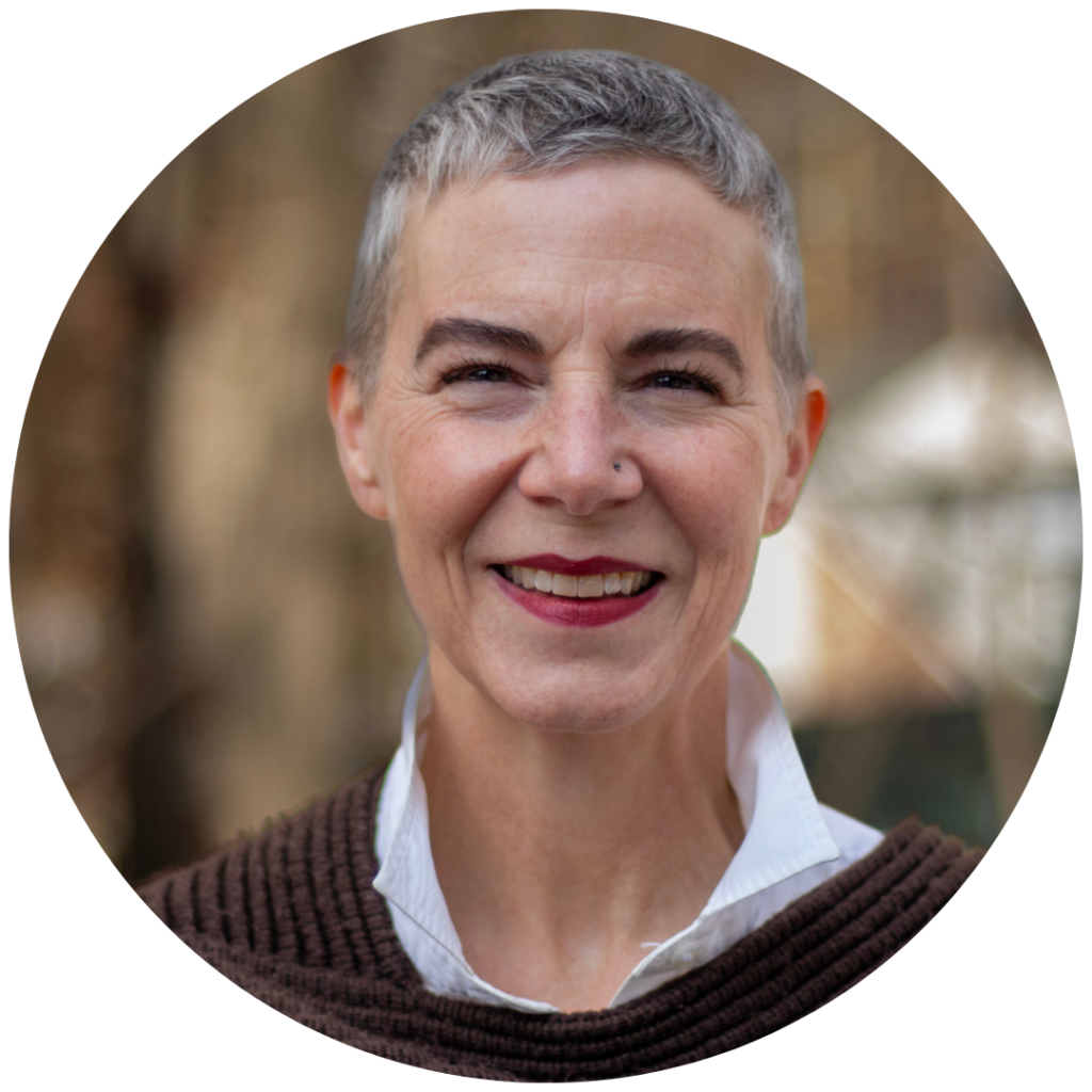 Smiling woman with short gray hair, wearing a white collared shirt and brown sweater, outdoors.