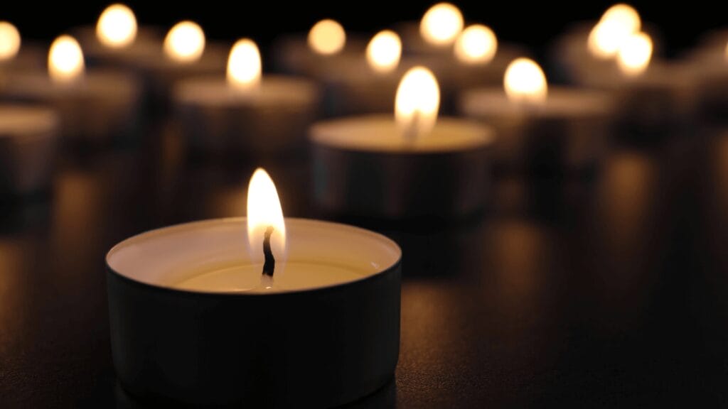 Several small tealight candles burning with soft, warm flames on a dark surface.