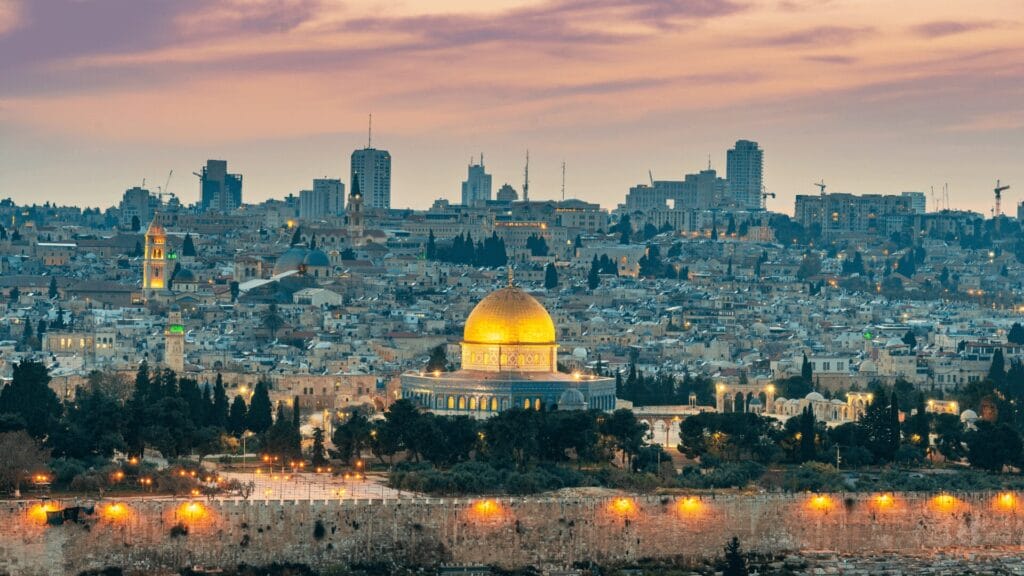 View of Jerusalem at sunset, featuring the golden Dome of the Rock and city skyline in the background.