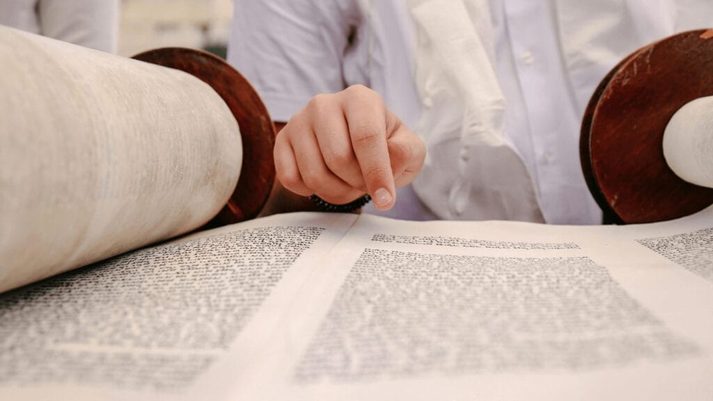 A person points at text on a Torah scroll, reading closely during a religious ritual.