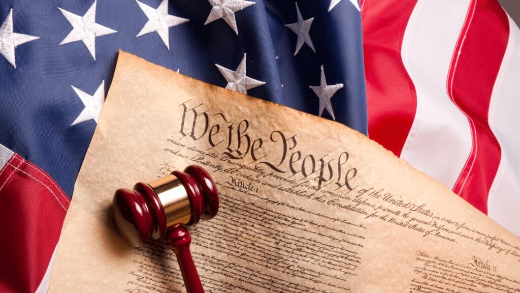 A gavel rests on the U.S. Constitution with the American flag in the background.