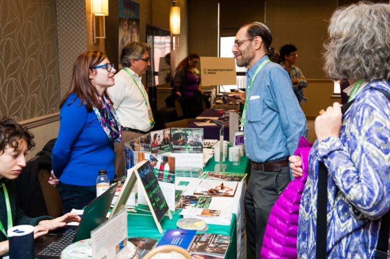 People chatting at a busy booth during a professional indoor event or conference.
