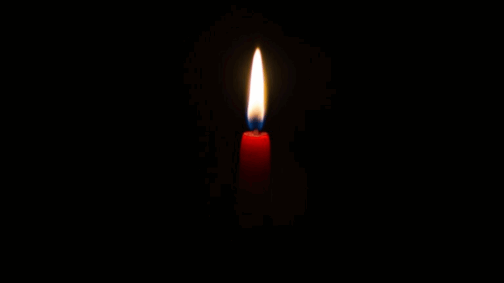 A single red candle burns brightly in the darkness with a small yellow flame.