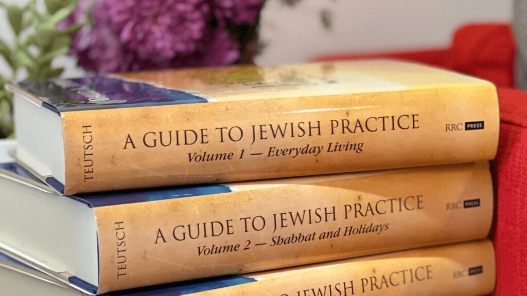 Two books titled A Guide to Jewish Practice stacked, with flowers blurred in the background.