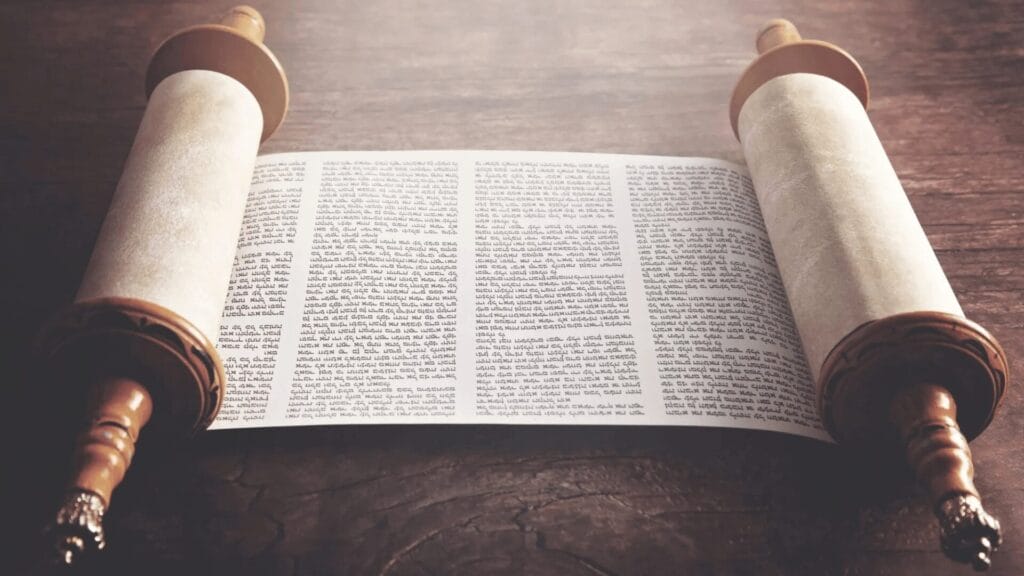 Ancient Torah scroll unfurled on a wooden table, with text visible across the parchment.