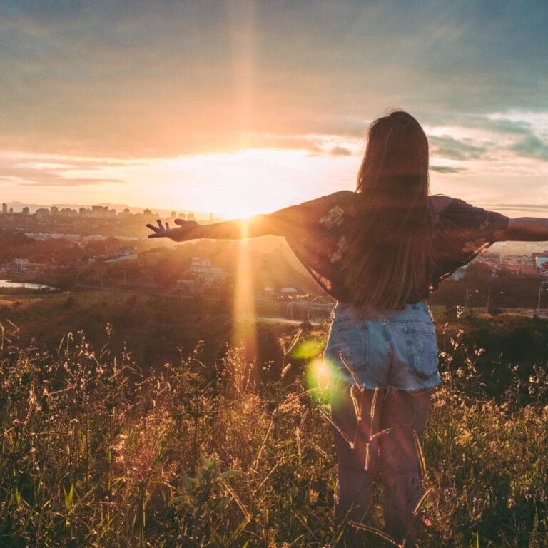 A woman standing in a field with her arms out.