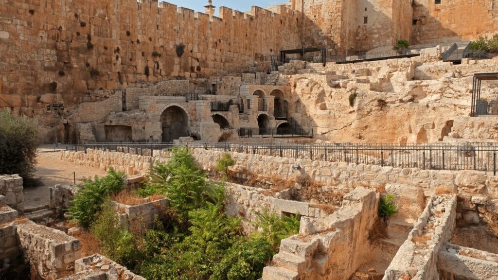 Ancient temple ruins in Israel beside a large fortified wall with greenery growing among the stones.