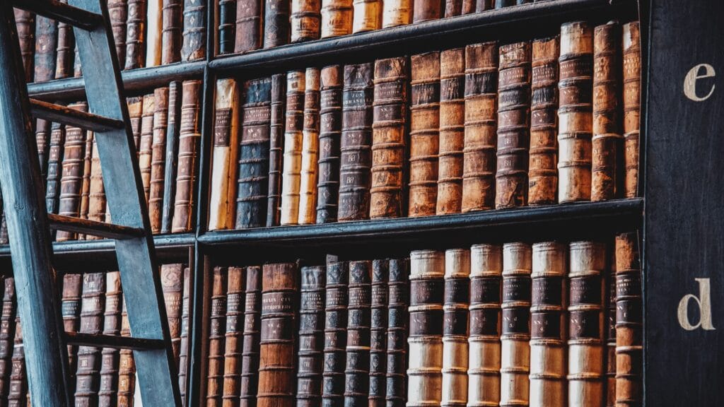 Wooden ladder beside shelves filled with rows of old, leather-bound books in a library.