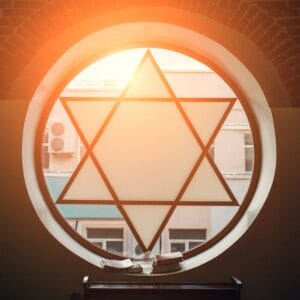 A round window with a Star of David design, sunlight shining through, books on a ledge below.