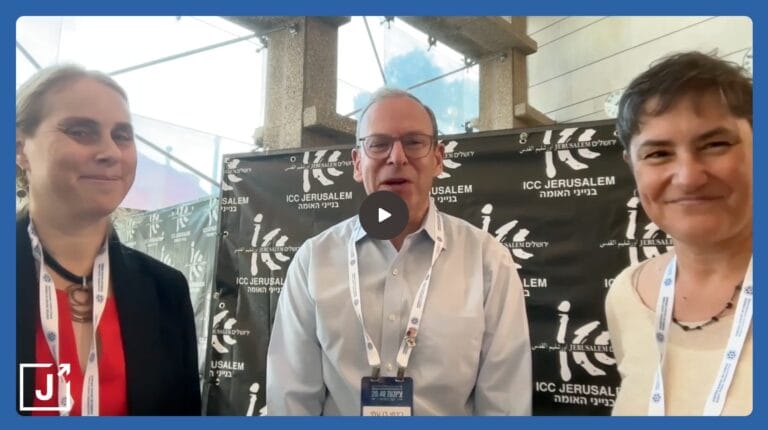Three people stand and smile in front of an ICC Jerusalem event backdrop inside a modern building.